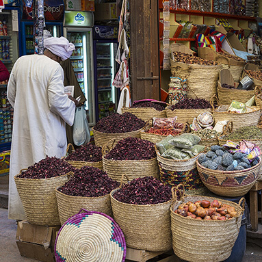 Egyptian market with a man standing with his back towards the camera, baskets filled with fruit and dried items.
