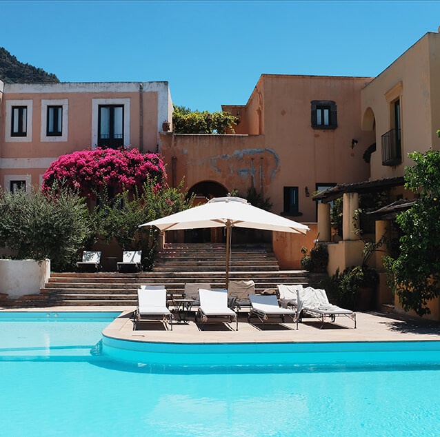 Buildings overlooking a swimming pool with white loungers at Hotel Signun in Salina, Italy.