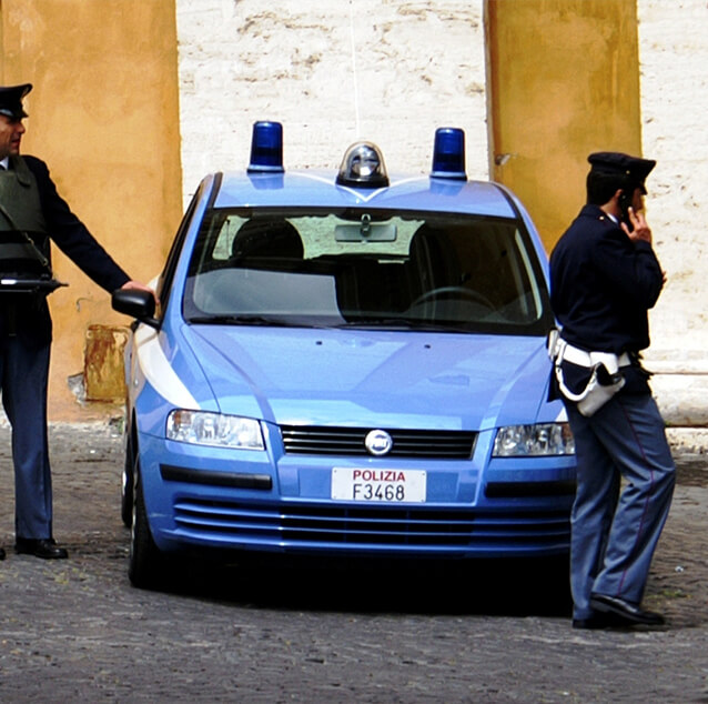 Two police officers standing next to a blue police car.