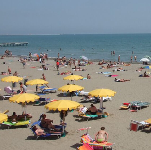 People on the beach siting under yellow umbrellas with the sea in the background.