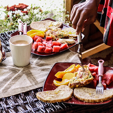 Colourful and delicious breakfast buffet on wheat bread with pieces of watermelon on the side and a hand putting an omelette on wheat bread with a fork.