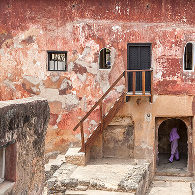 Kenyan heritage site, old building with stairs and chipped paint and a woman walking into an open doorway.