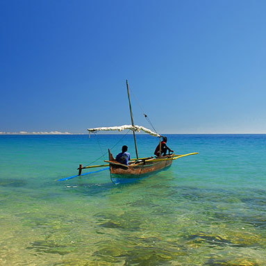 Two men in a small boat floating on shore.