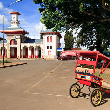 Red rickshaw on the street with a building in the background.