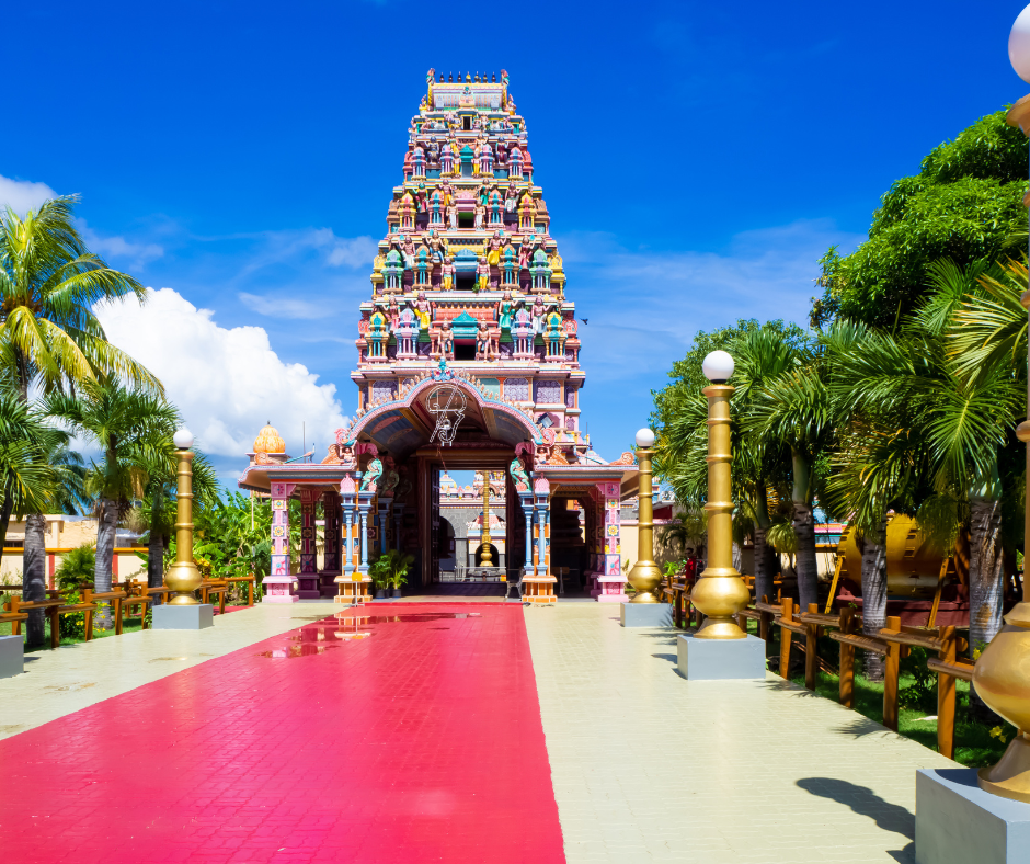 Pink and white Hindu temple with a tree on the front right side of the temple.