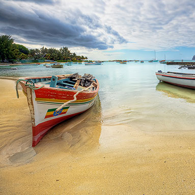 Green palm trees leaning into blue seashore on white beach.