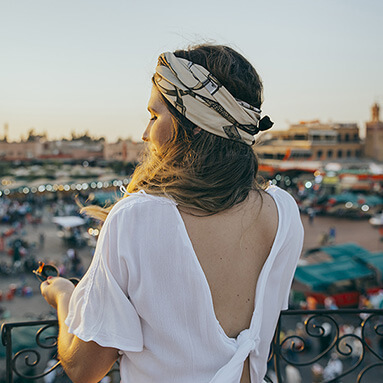 Woman standing on balcony of building overlooking Moroccan market.