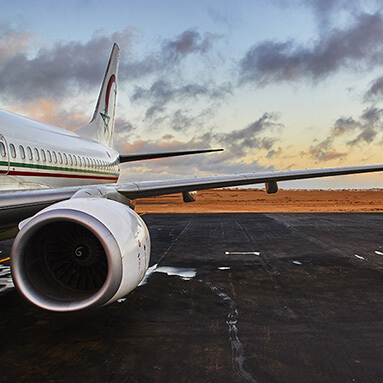 Side view of stationery Moroccan plane wing and tail, with blue and orange sunset in distance.