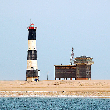 Black, white and red Namibian lighthouse next to wooden communication house.