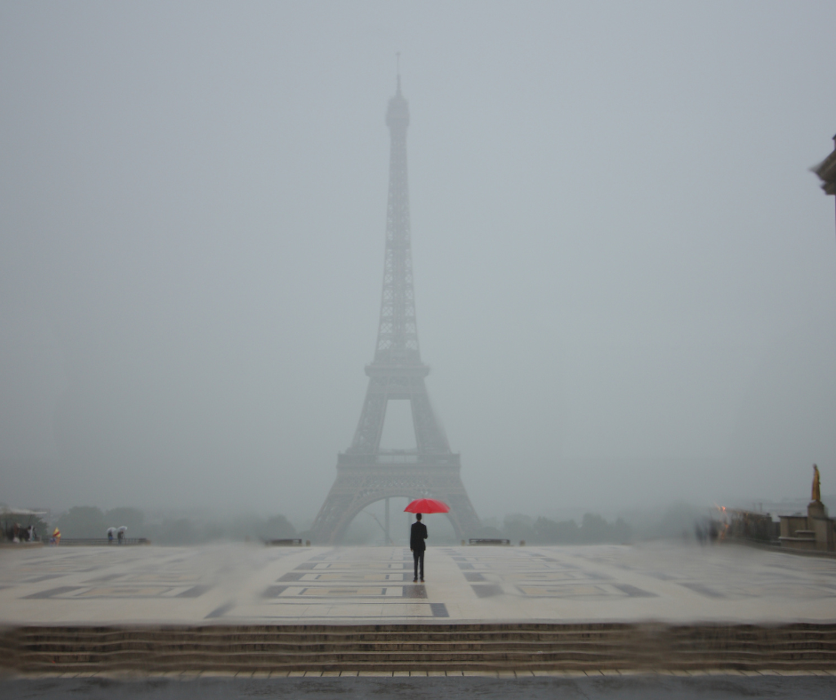 Two people under a red umbrella with the Eiffel tower in the background.