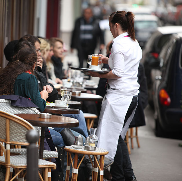People sitting outside a restaurant with a waitress serving them