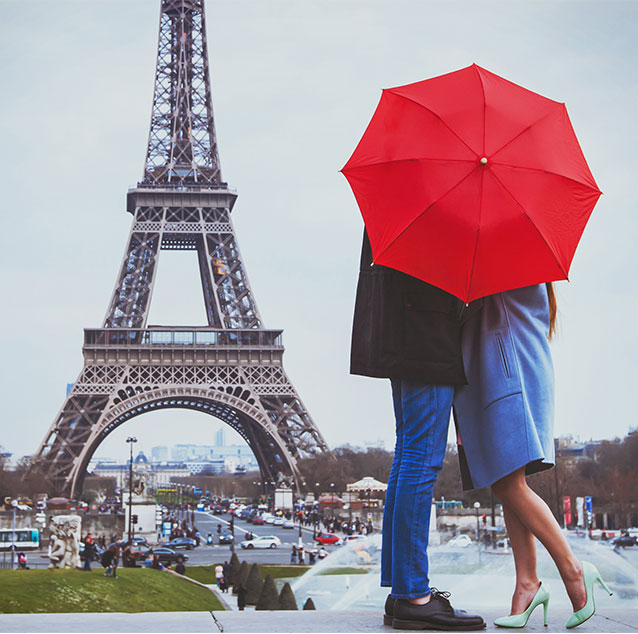 Two people under a red umbrella with the Eiffel tower in the background.