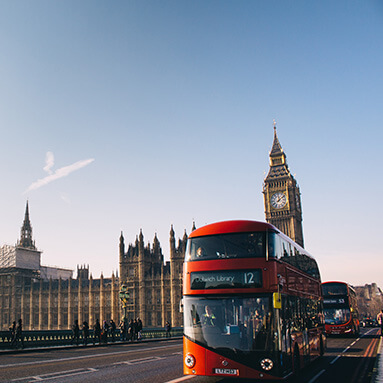 Red double decker London buses driving pass the Palace of Westminster. 