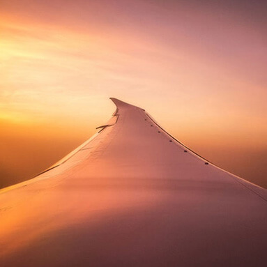 Aeroplane wing over orange clouds in high altitude with sunset.
