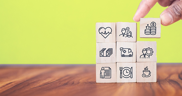 Alt text: Hand arranging wooden blocks with icons representing various aspects of medical aid Alt text: Hand arranging wooden blocks with icons representing various aspects of medical aid