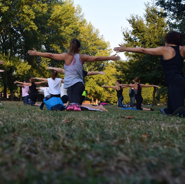 Back view of group of people doing pilates in park.