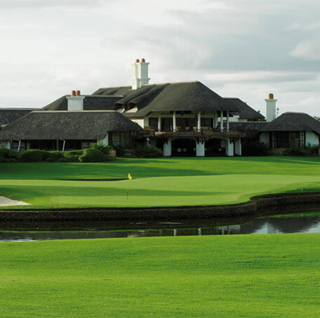 Beautiful image of Leopard Creek Golf Course , thatched-roof club house with white walls and creek in front of club house.