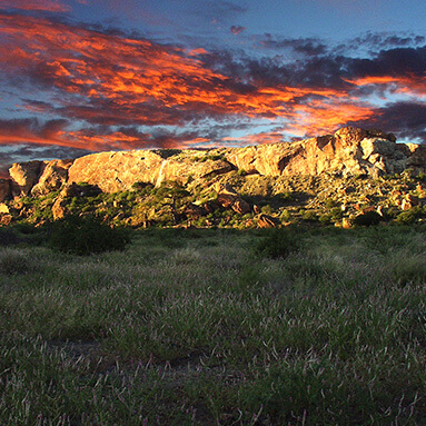 Red sunset with cloudy, blue skies, over mapungubwe hills and grass and trees.