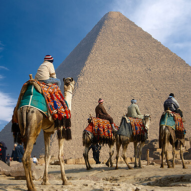 Men with colourful clothing, riding on camels in front of the pyramid.