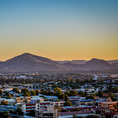 Topographical view of neat, urban Windhoek buildings, with a picturesque blue and orange sky and mountain in distance.